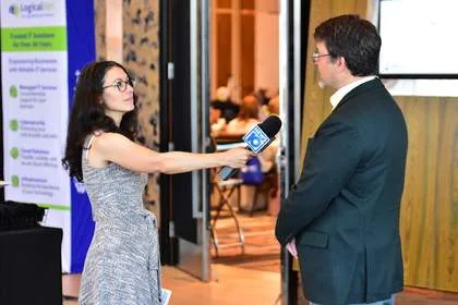 Reporter interviewing attendee at Tech Valley Cybersecurity Symposium, LogicalNet display in background
